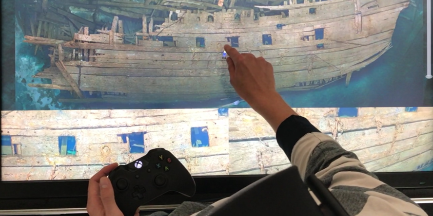 Jemand navigiert mit dem Zeigefinger und mittels Conroller in der digitalen Darstellung eines Schiffswracks.