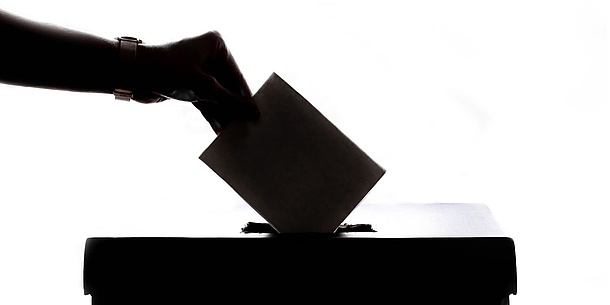 Eine Hand wirf einen Zettel in einen Wahlurne.
