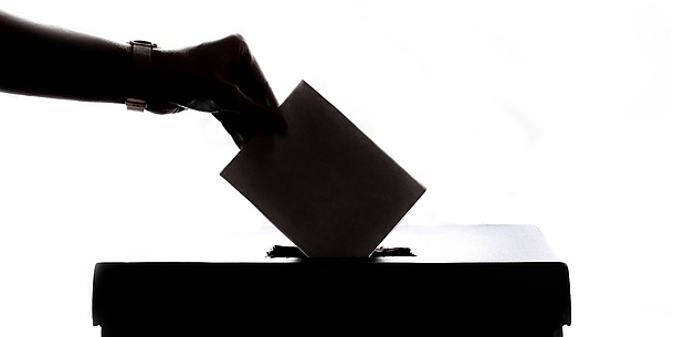 A hand throws a note into a ballot box.