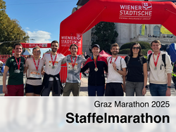 Eine lachende Gruppe von sieben Finishern mit Medaillen posiert beim Graz Marathon 2025 Staffelmarathon vor dem roten Wiener-Städtische-Zieleinlaufbogen.