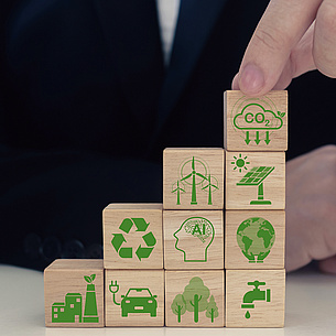Hand stappelt kleine Holzwürfel mit grünen Icons zum Thema Zero Carbon