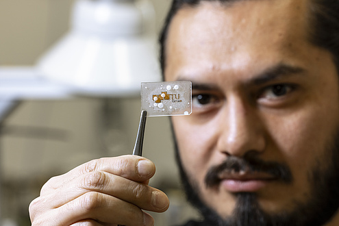 A man holds up a frozen piece of glaze using a tweezers.