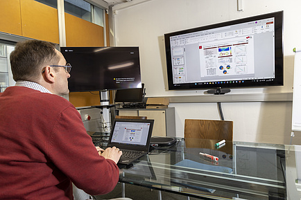 A man at a desk looks at a monitor on the wall