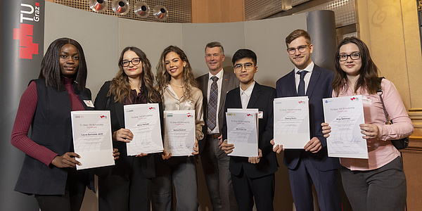 Seven people are standing next to each other, holding certificates in their hands and looking at the camera.