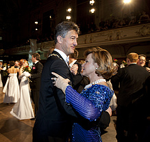 Ein Mann im schwarzen Anzug und eine Frau in einem blauen Ballkleid tanzen. 