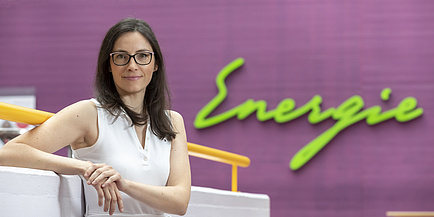 A woman smiles into the camera. With her elbow she leans on a wall. Behind her the word Energy can be seen.