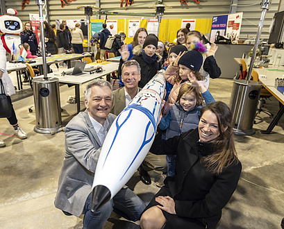 A woman, two men and several kids hold a rocket together.