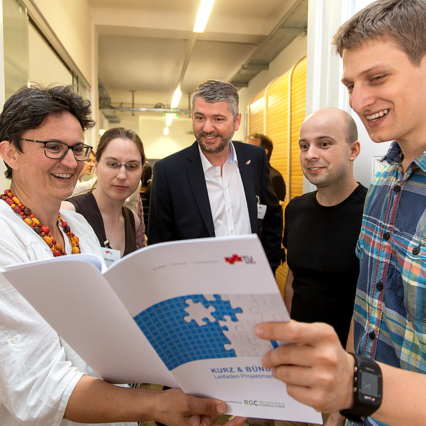 Mehrere Personen betrachten einen Leitfaden für Projektmanagement der TU Graz. Bildquelle: Lunghammer – TU Graz