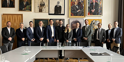 A group of people stand in front of a wall of portraits and smile at the camera.