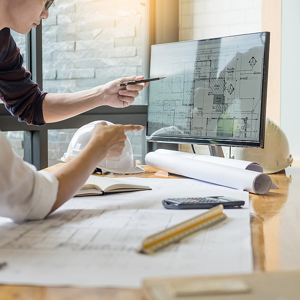 Arbeitstisch mit Bildschirm und Bauplänen.