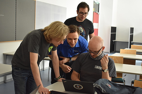 vier junge Männer beugen sich bei den Linuxtagen über ein Notebook und arbeiten gemeinsame
