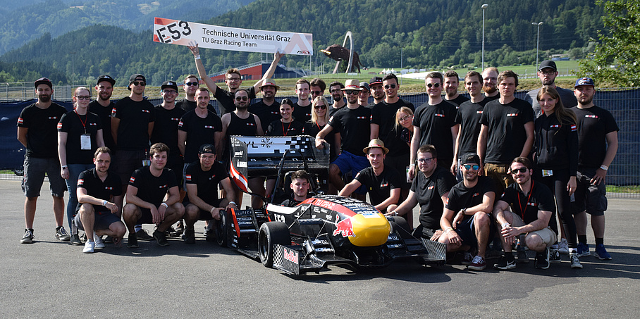 A group of young people around a race car