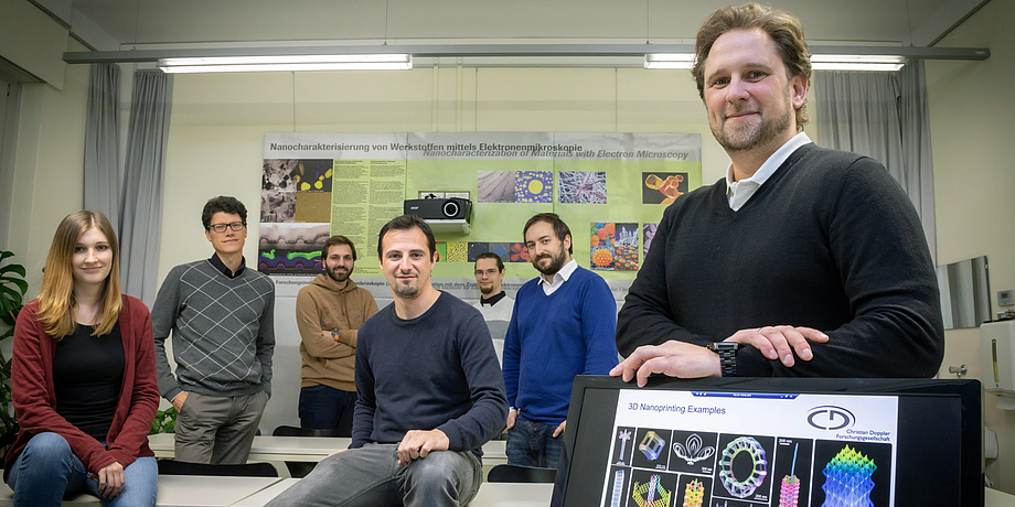 Group of people stands next to a screen with images of nanostructures on it, a poster on nanoanalytics behind them