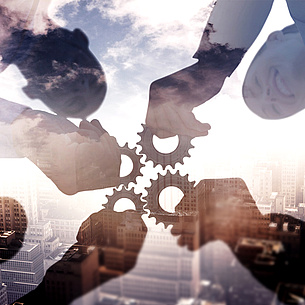 People holding together gear wheels. A building in the background. Photo source: vectorfusionart - Fotolia.com