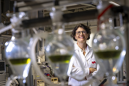 Smiling woman in a lab coat behind glass containers filled with coloured liquid.