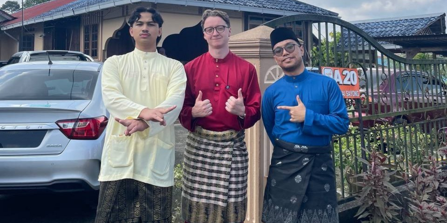 Three young men in traditional Malaysian robes smile at the camera.