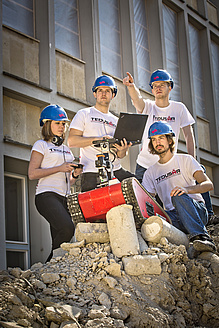 Three men and a woman with a small tracked vehicle on a stone hill.