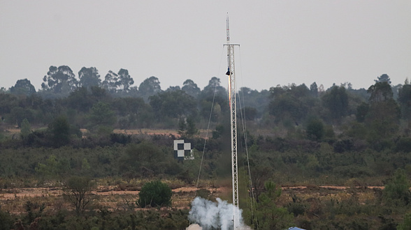 A rocket launches from a bushy plain.