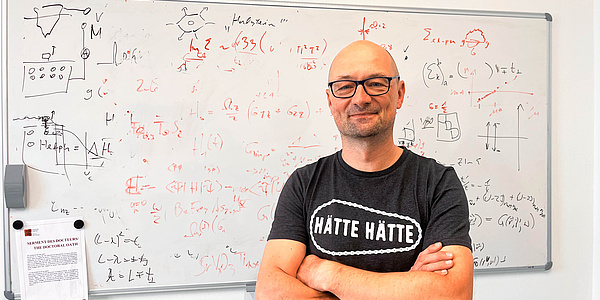 Ein Mann lehnt an einem vollgeschriebenen Whiteboard.
