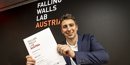 A smiling man holds a document that says he is the winner