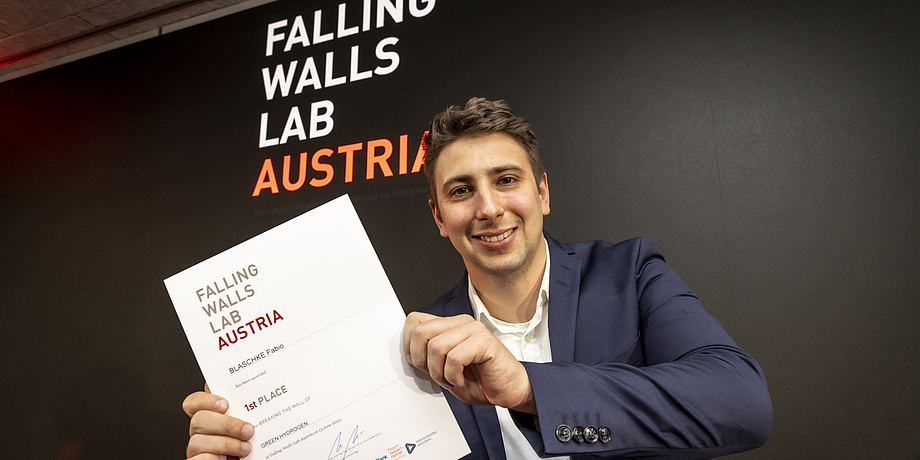 A smiling man holds a document that says he is the winner