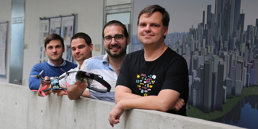 Four man are standing in front of a concrete wall.