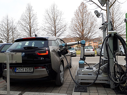 A blue electric vehicle is charged by the robot. The arm of the robot is plugged into the vehicle socket.