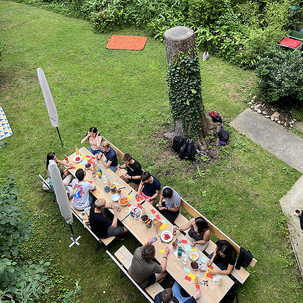 Meschen sitzen an einem langen Tisch in einem Garten