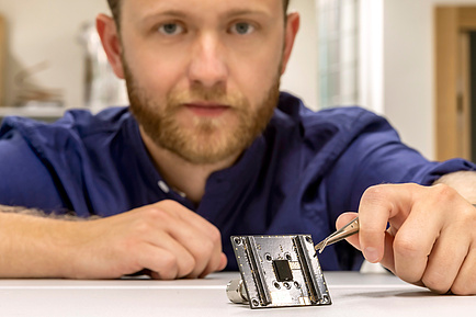 TU Graz researcher holds a one-cent coin with tweezers, in front of it a small sensor
