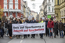 Menschenmenge, die demonstriert. Sie halten ein Plakat in den Händen, auf dem steht: Unis auf Sparflamme=Zukunft auf Sparflamme. 