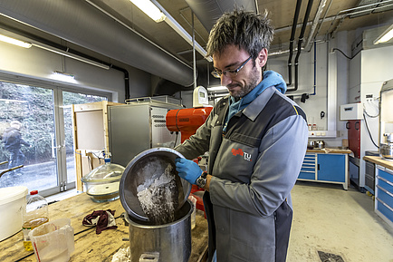 Man standing in the laboratory pouring a solid substance from one container to another.