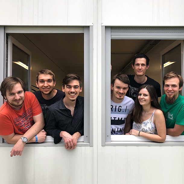 7 young people smiling out of a window