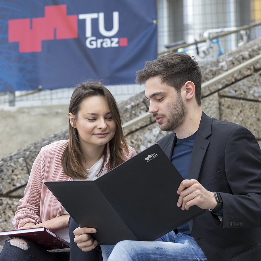 A young woman and a young man read a TU Graz brochure.
