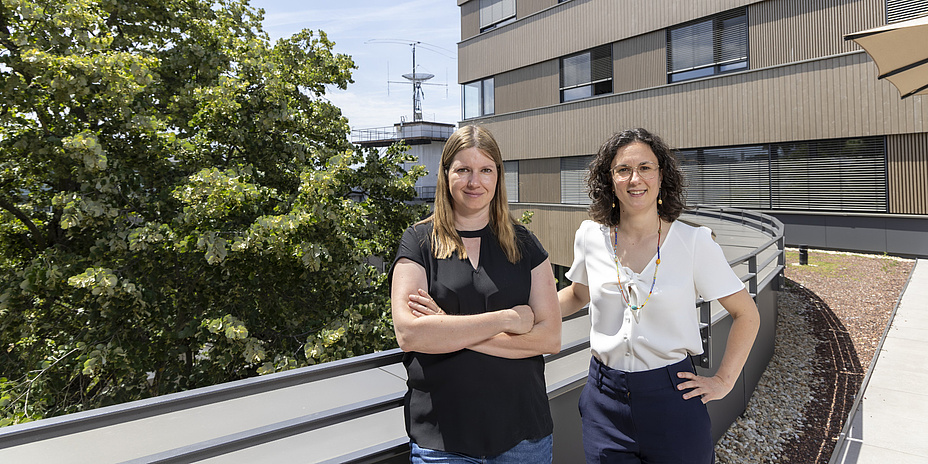 Two women are standing on a terrace, smiling at the camera.