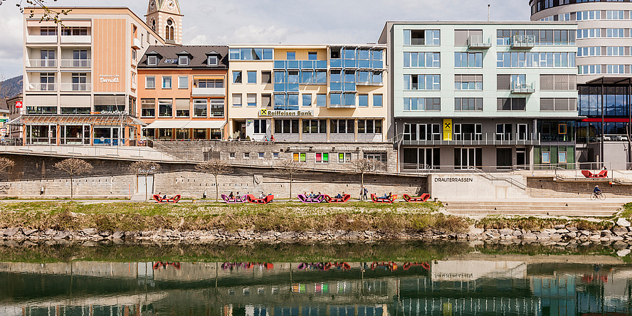 Zu sehen ist ein Stadtbild von Villach, die Draufassade und links davon der Kirchturm.