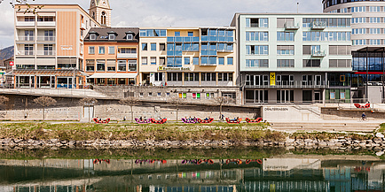 Zu sehen ist ein Stadtbild von Villach, die Draufassade und links davon der Kirchturm.