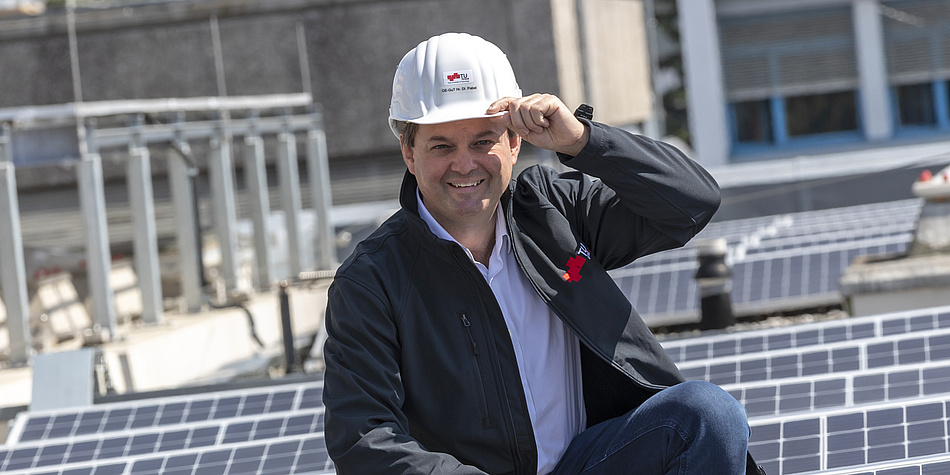 Ein Mann in schwarzer Jacke und mit weißem Helm befindet sich inmitten einer Photovoltaik-Anlage.