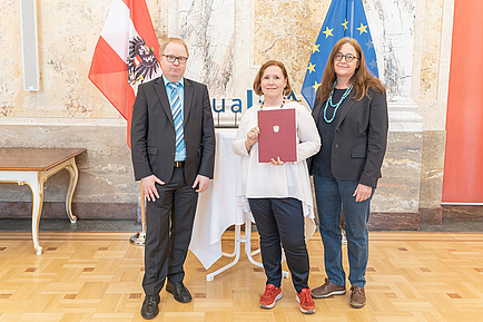 Ein Mann und zwei Frauen vor zwei Fahnen