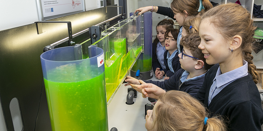 Several children look at a glass structure filled with liquid.