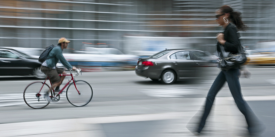 Eine gehende Frau, ein Radfahrer und ein Auto