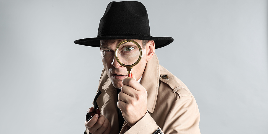 Male detective with smoking pipe looking through magnifying glass on grey background