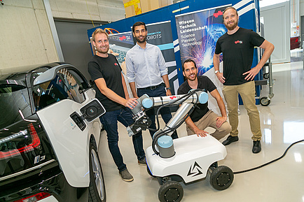Vier Männer vor einer Plattform auf Räder mit Roboterarm