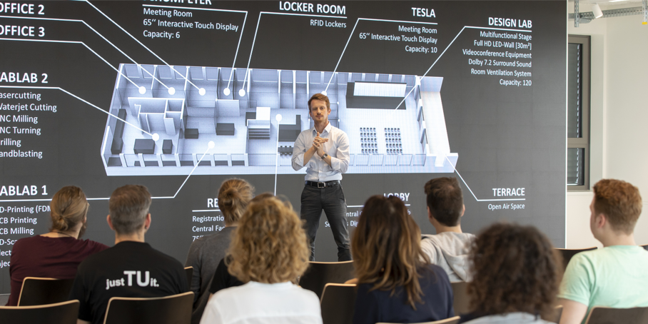 Several interested people listen to a man lecturing on stage in a lecture hall at Graz University of Technology.