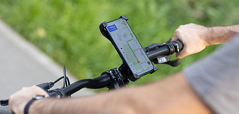 Ein Fahrradlenker, auf dem ein Smartphone angebracht ist, das eine Navigations-App auf dem Bildschirm hat.