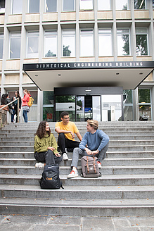 Drei Personen sitzen auf einer Treppe vor einem Gebäude.