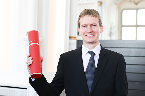 A man holds up a red document roll and smiles into the camera.