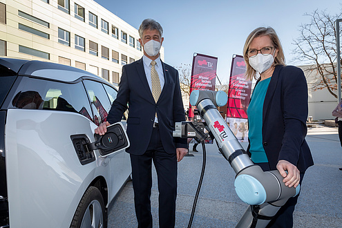 Mann und Frau neben einem E-Auto mit automatischem E-Laderoboter