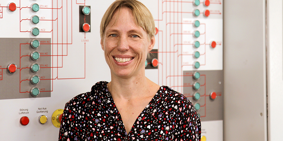 A woman in front of a wall with red and green buttons which are connected with red lines.