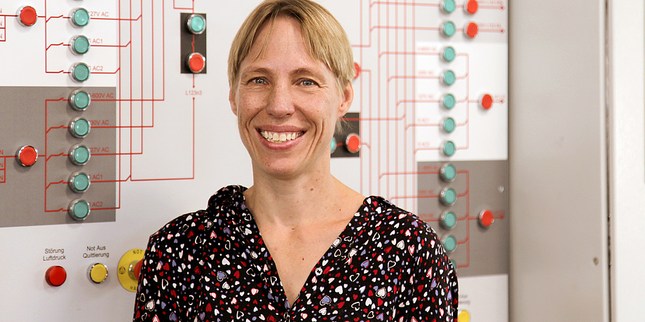 A woman in front of a wall with red and green buttons which are connected with red lines.