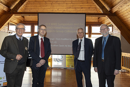 Four men in suits standing in front of a screen.